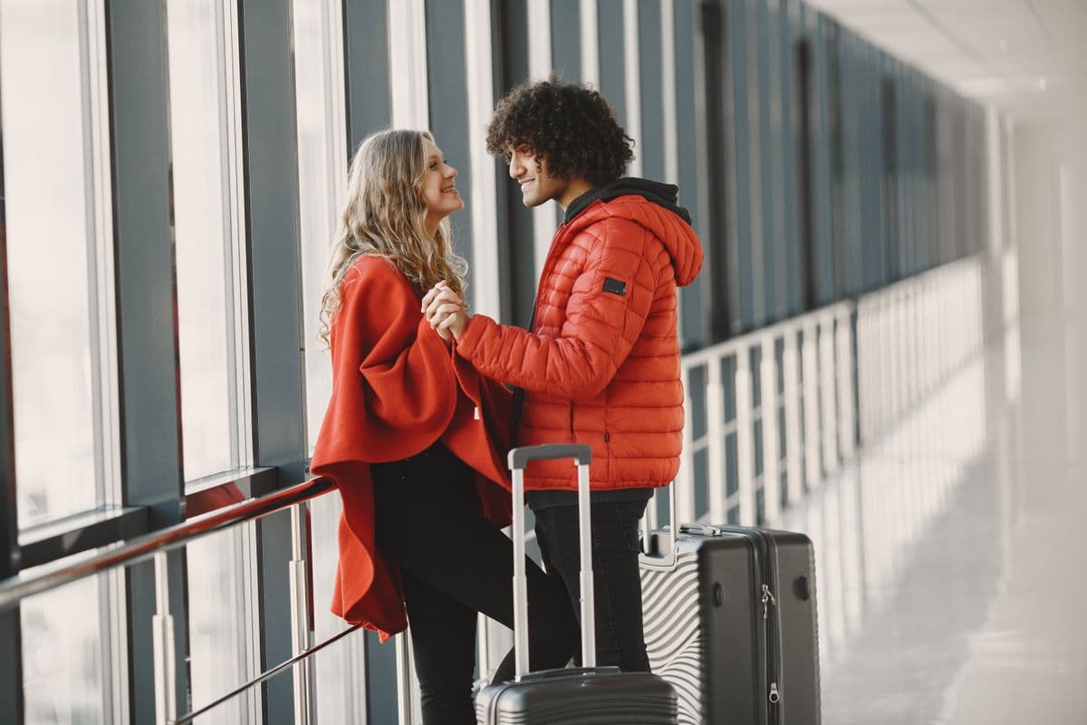 Two travellers in red coats smiling together in a bright airport walkway