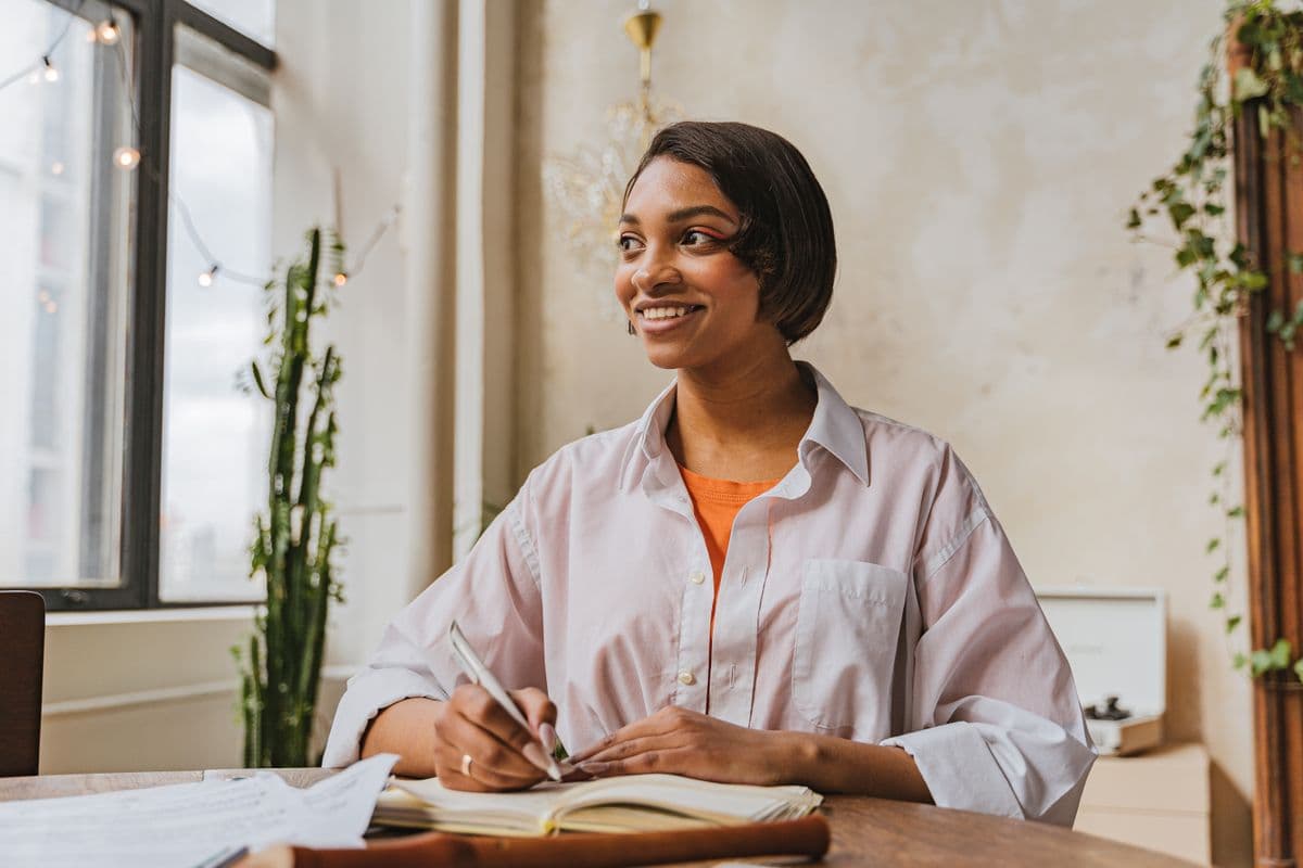 Person smiling as they work through paperwork at a sunlit table at home