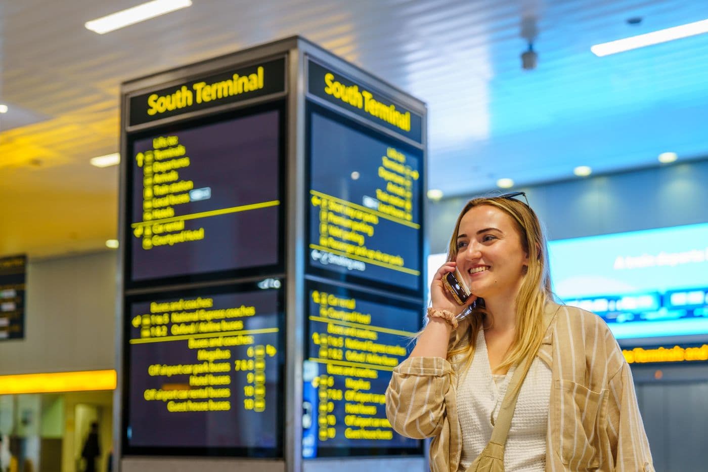 Smiling passenger on the phone beside the bright yellow information boards in an airport terminal